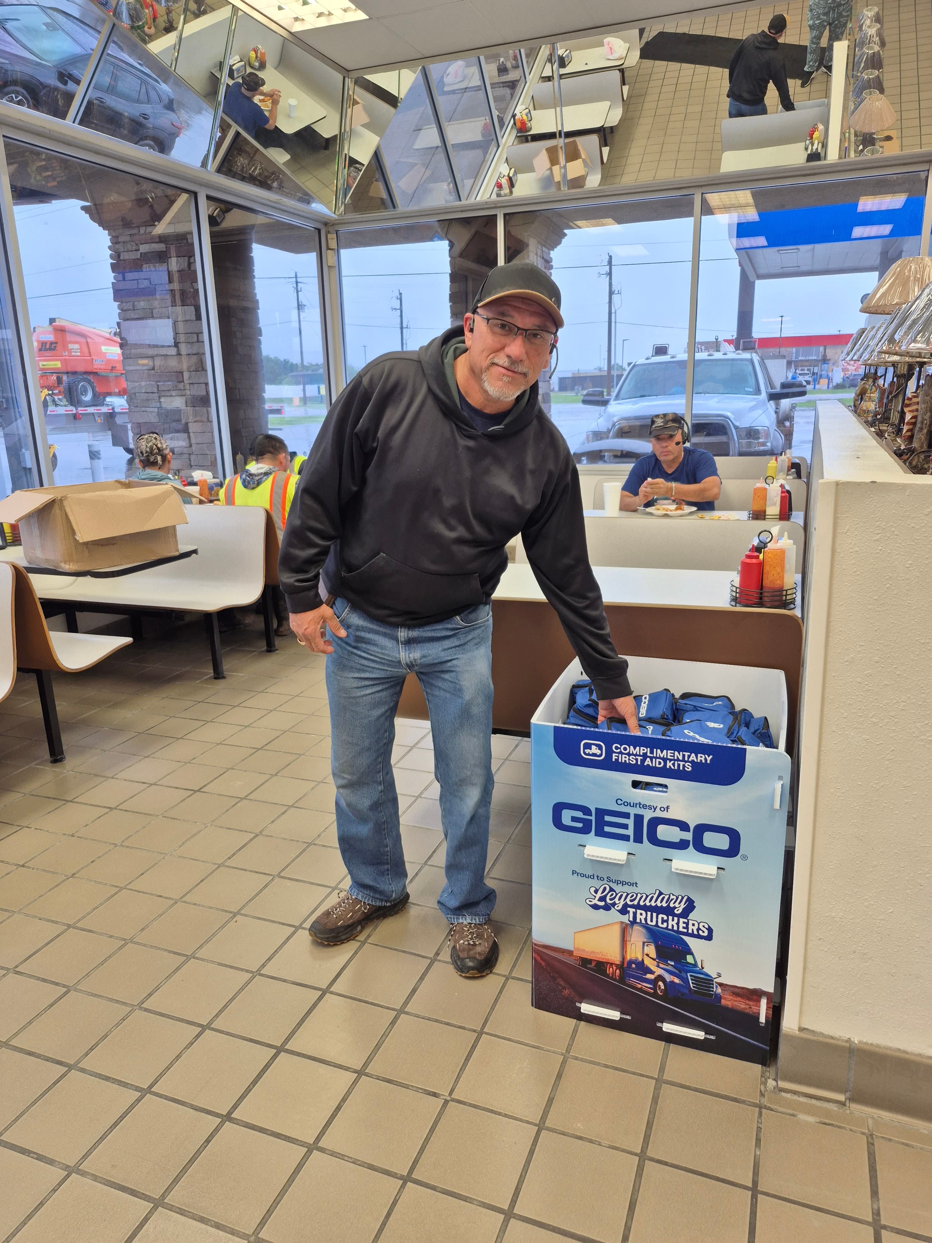 A customer beside an insurance-brand display offering complimentary first aid kits inside a truck stop